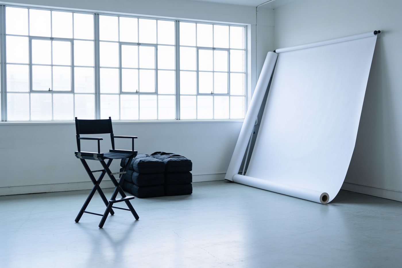 Aufgerollter Studiohintergrund, Sandsäcke und ein zusammengeklappter Stuhl in einem leeren Studio